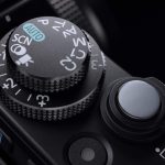 Palce wskazują najważniejsze elementy sterujące: włącznik i spust migawki na górnej ścianie aparatu i rolkę ponad uchwytem.